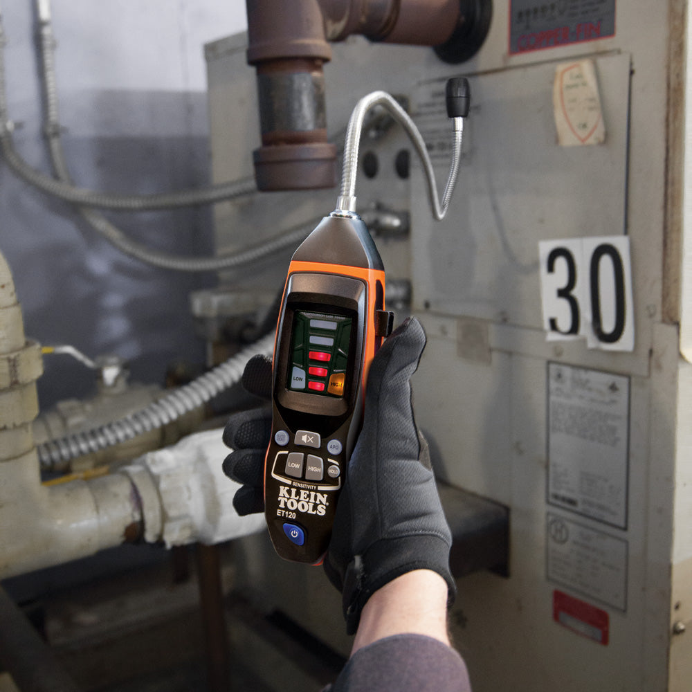 A professional technician holding an electronic natural gas leak detector near an appliance connection.